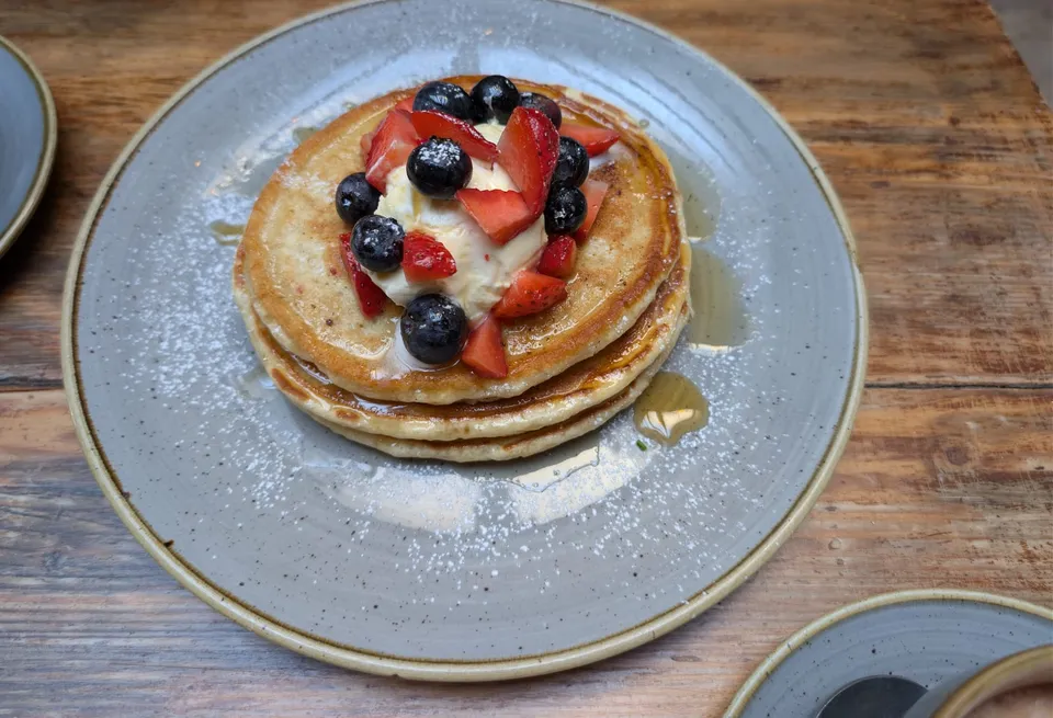 A stack of pancakes with berries, cream, and syrup