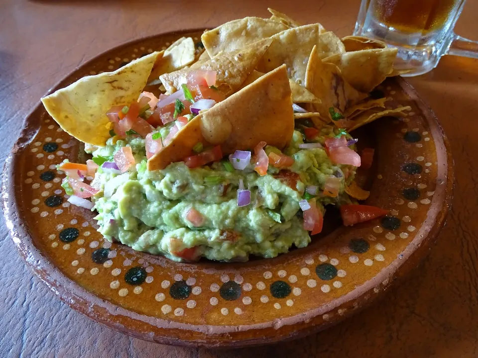 Chunky guacamole in a painted clay dish with tortilla chips
